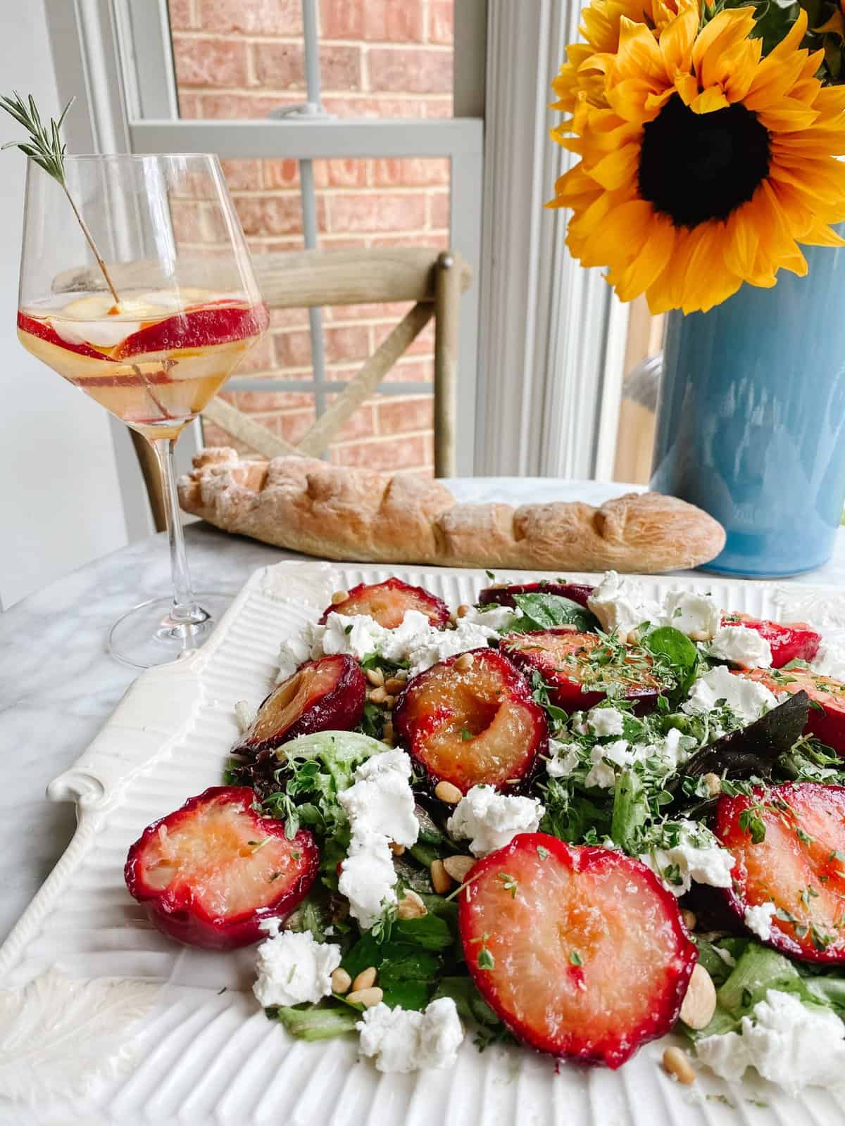 roasted plums, goat cheese salad with a glass of wine and a french baguette and a sunflower