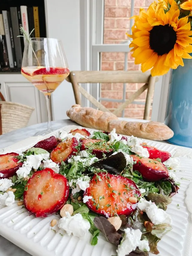 roasted plums, goat cheese and lemon thyme with a glass of rosé and a sunflower on a table