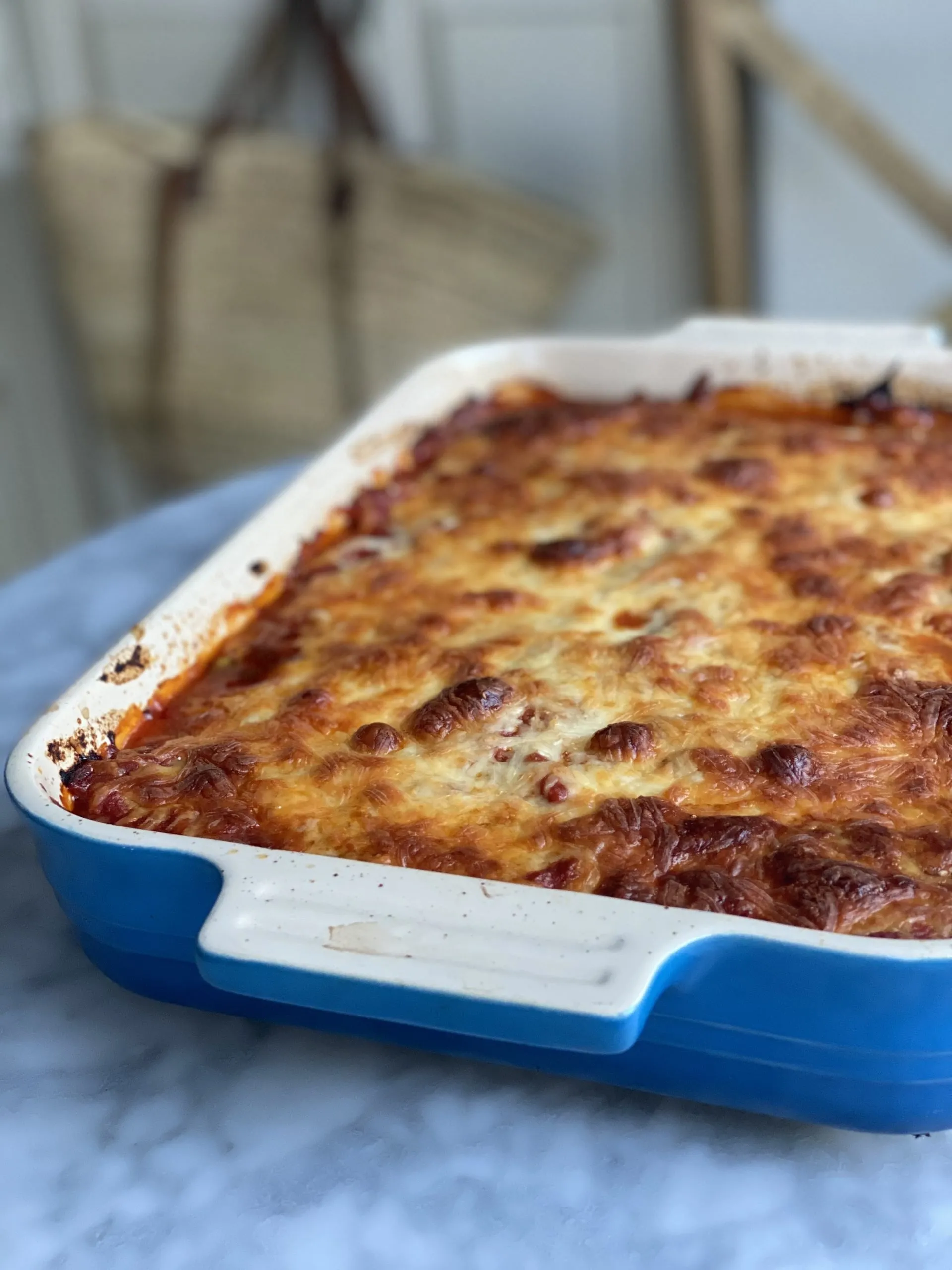 Eggplant Lasagna, crisp layer of baked cheese in a blue Le Creuset dish on a marble table