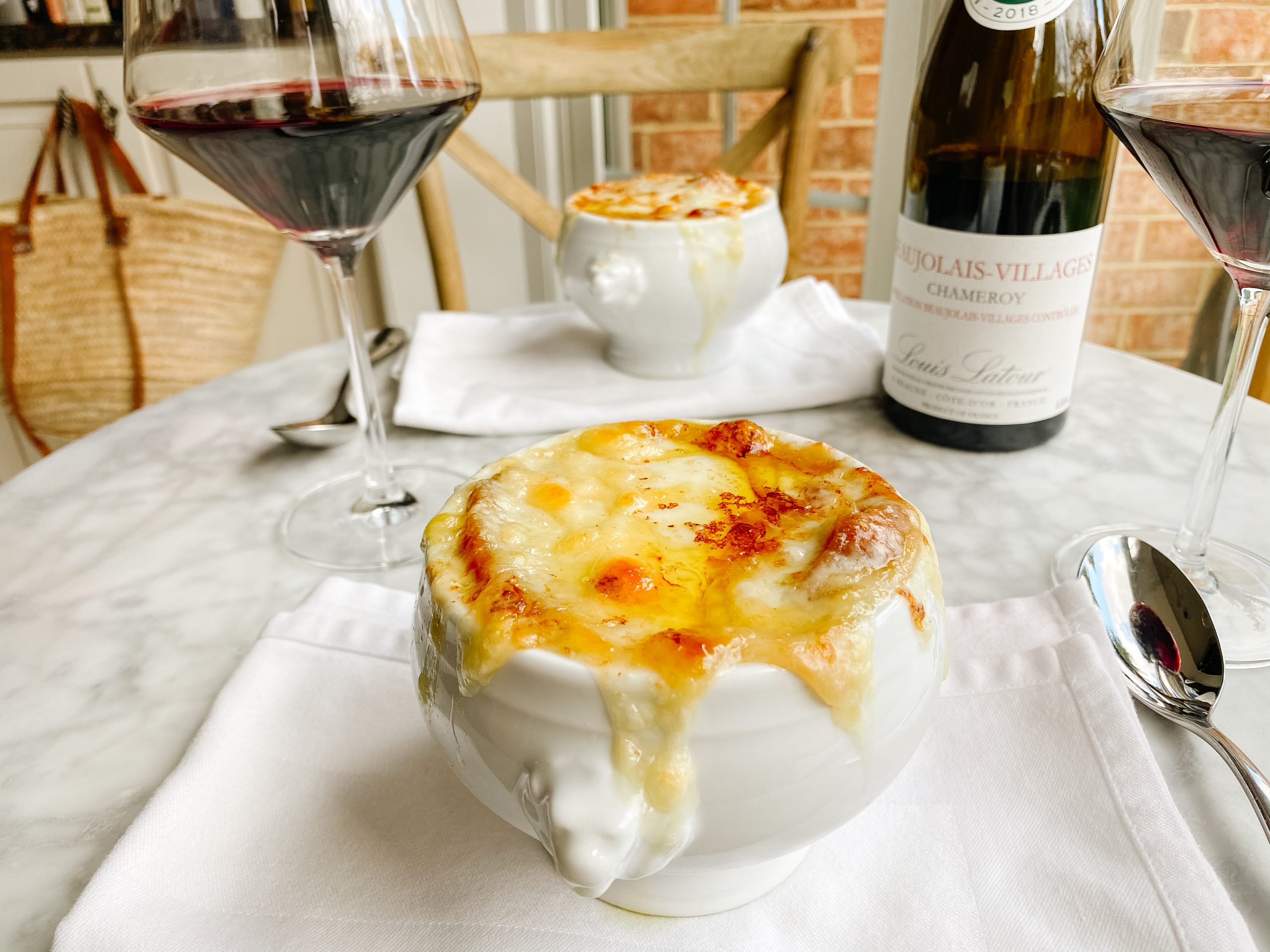 two bowls of french onion Soup on a table with wine