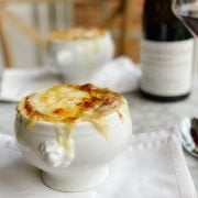french onion Soup gratinée in a white bowl with wine
