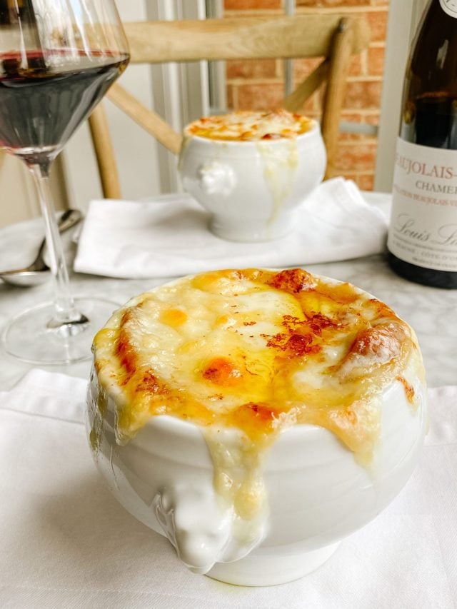 two bowls of french onion Soup on a table with wine