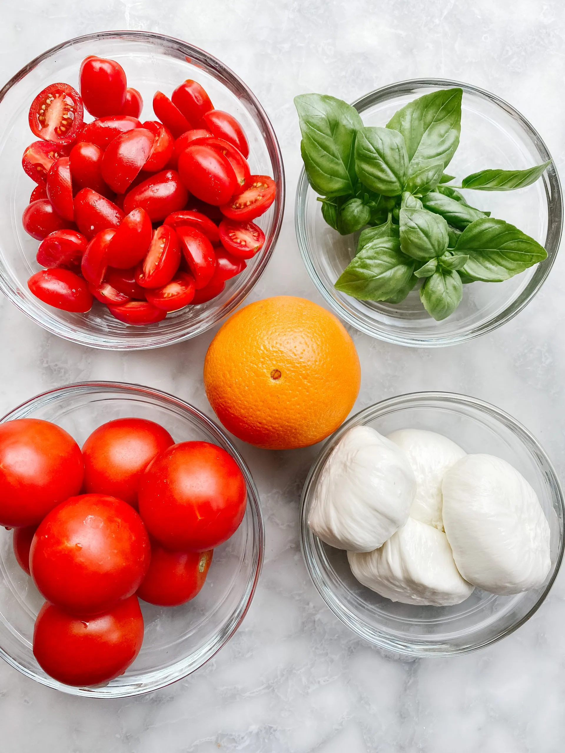 4 glass bowls filled with tomatoes, basil and burrata cheese with an orange in the middle