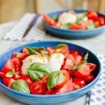 tomato basil salad in a blue bowl on a marble table with a napkin and a knife