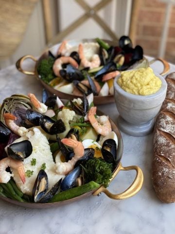 2 copper plates with Le Grand Aรฏoli, shrimp, cod, fresh vegetables, mussels a french baguette and aรฏoli and a baguette