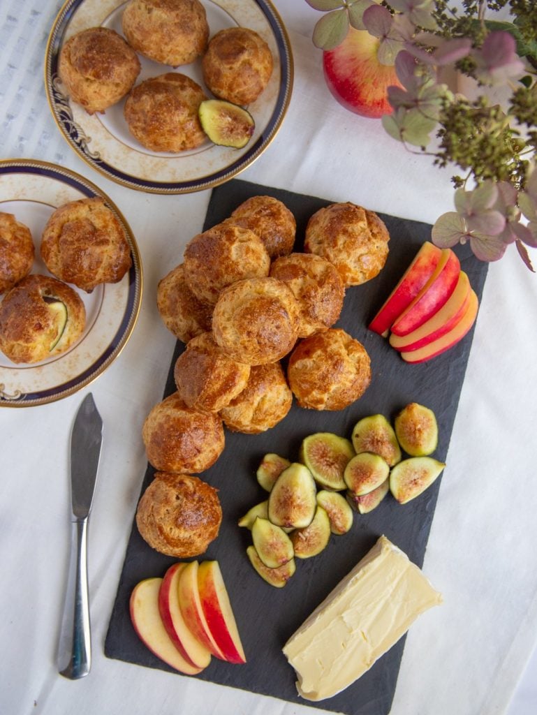 Gougeres on a plate with apples and figs and a slice of cheese