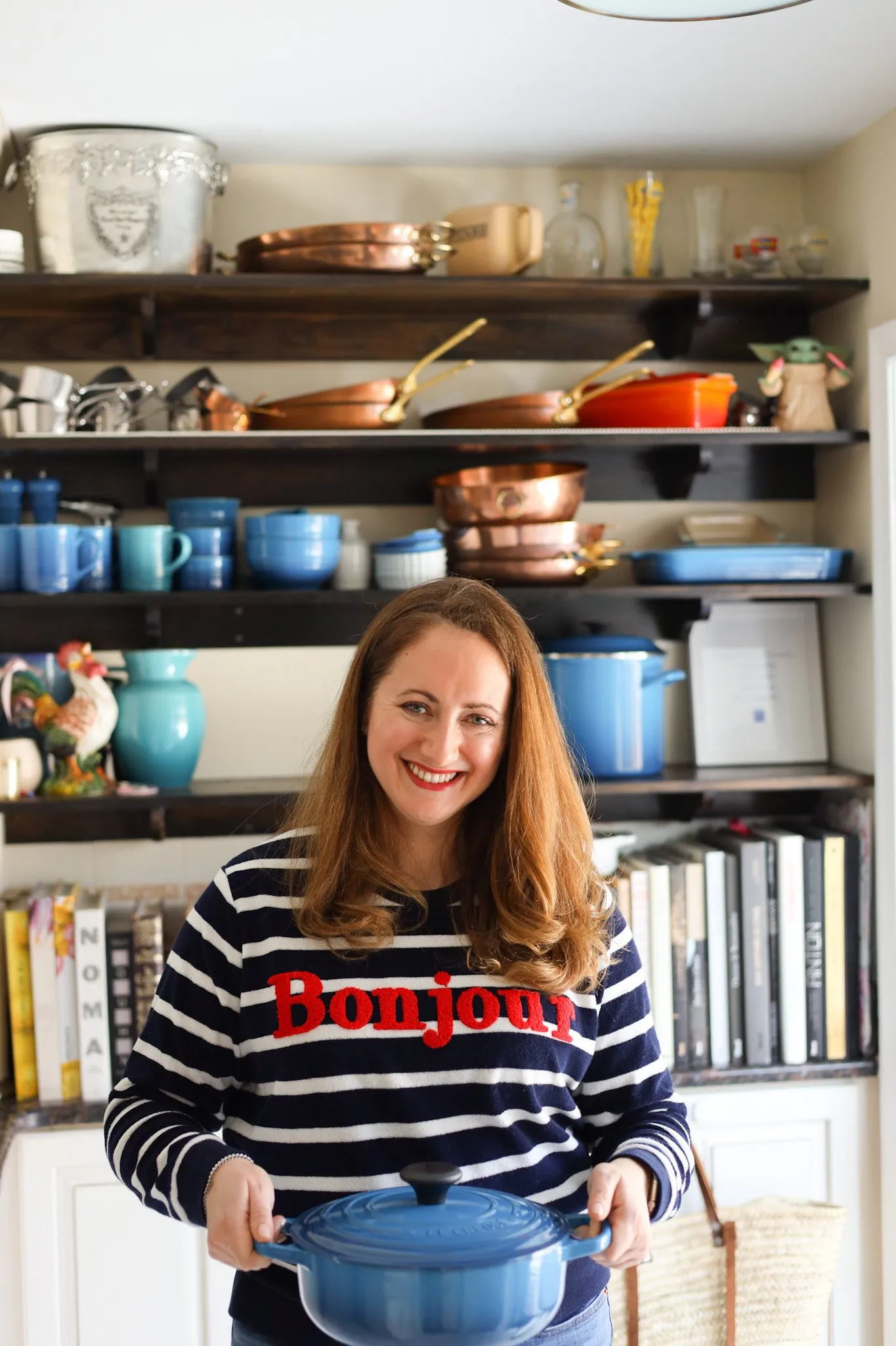 Le Chef's Wife in her kitchen in front of a row of pots and pans