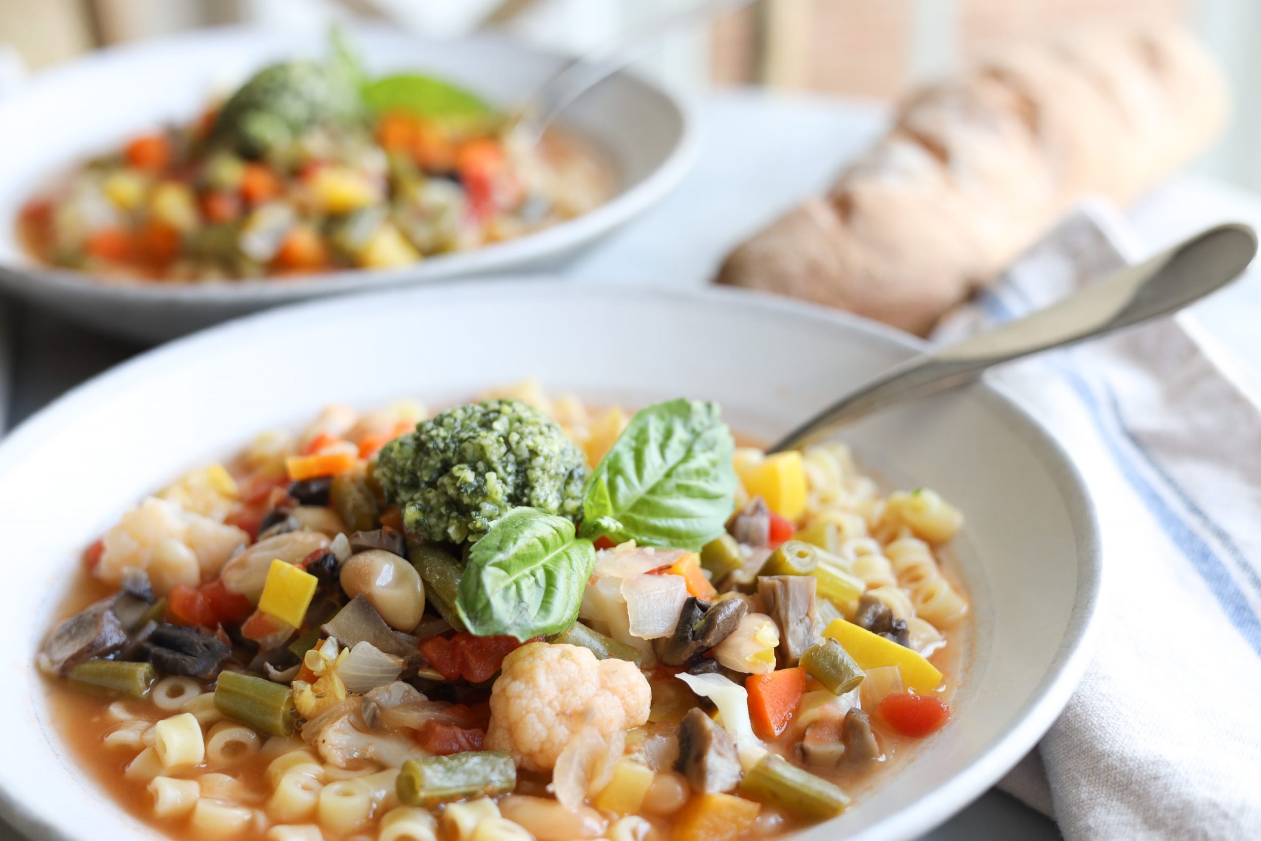 vegetarian minestrone with homemade pesto in 2 bowls and a baguette 2