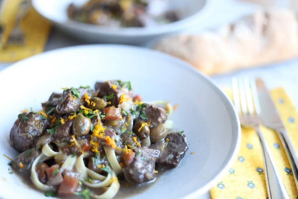 Daube provençal in a white bowl - beef stew with fettucine and olives on a white plate