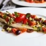 Branzino on a plate with Vierge Sauce made of tomatoes, capers, shallots, olives and basil