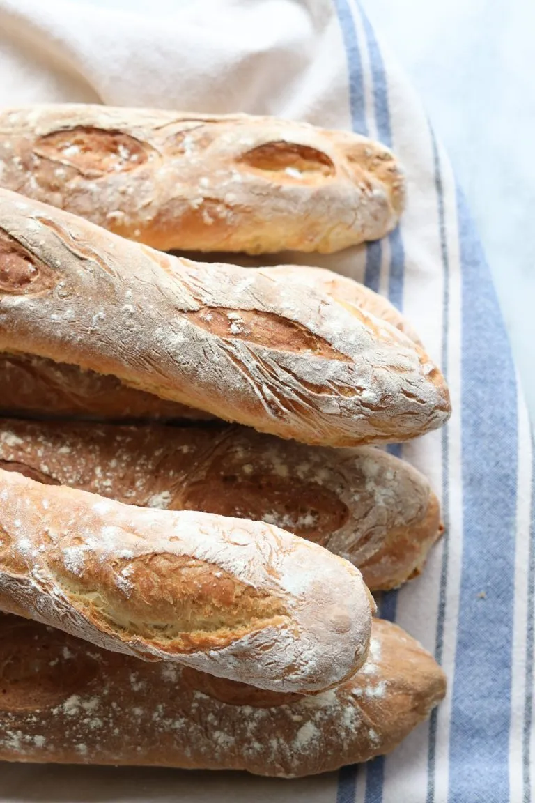 homemade French baguettes piled up on a striped cotton towl