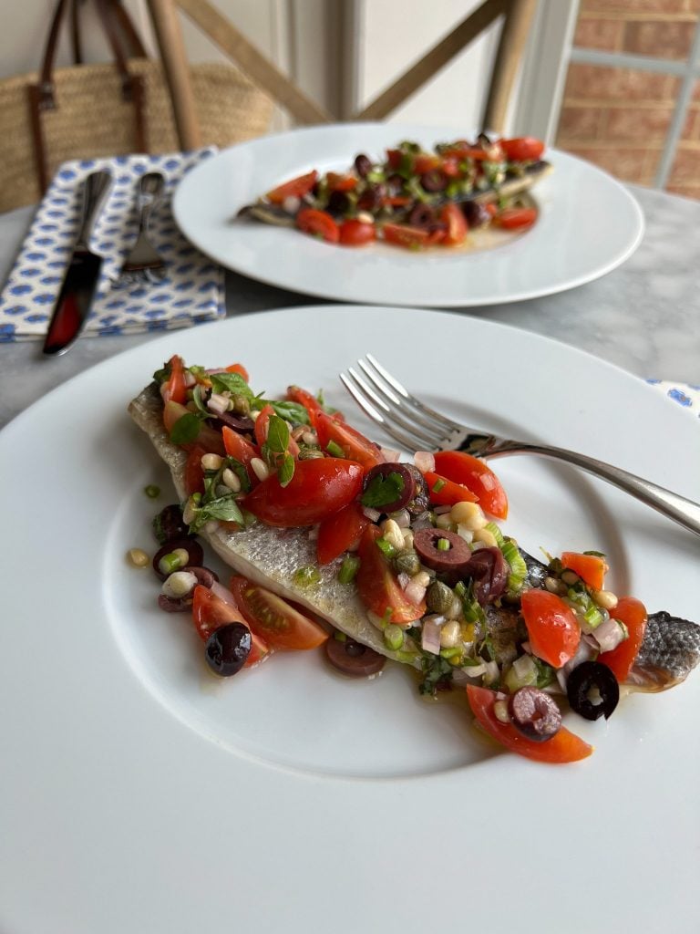 Branzino on a plate with Vierge Sauce made of tomatoes, capers, shallots, olives and basil