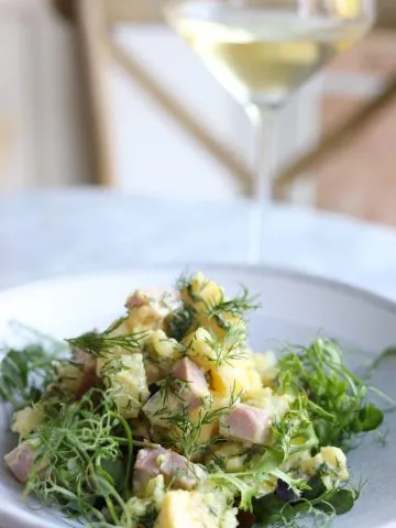 Parisian Potato salad on a plate with mixed greens and a glass of white wine