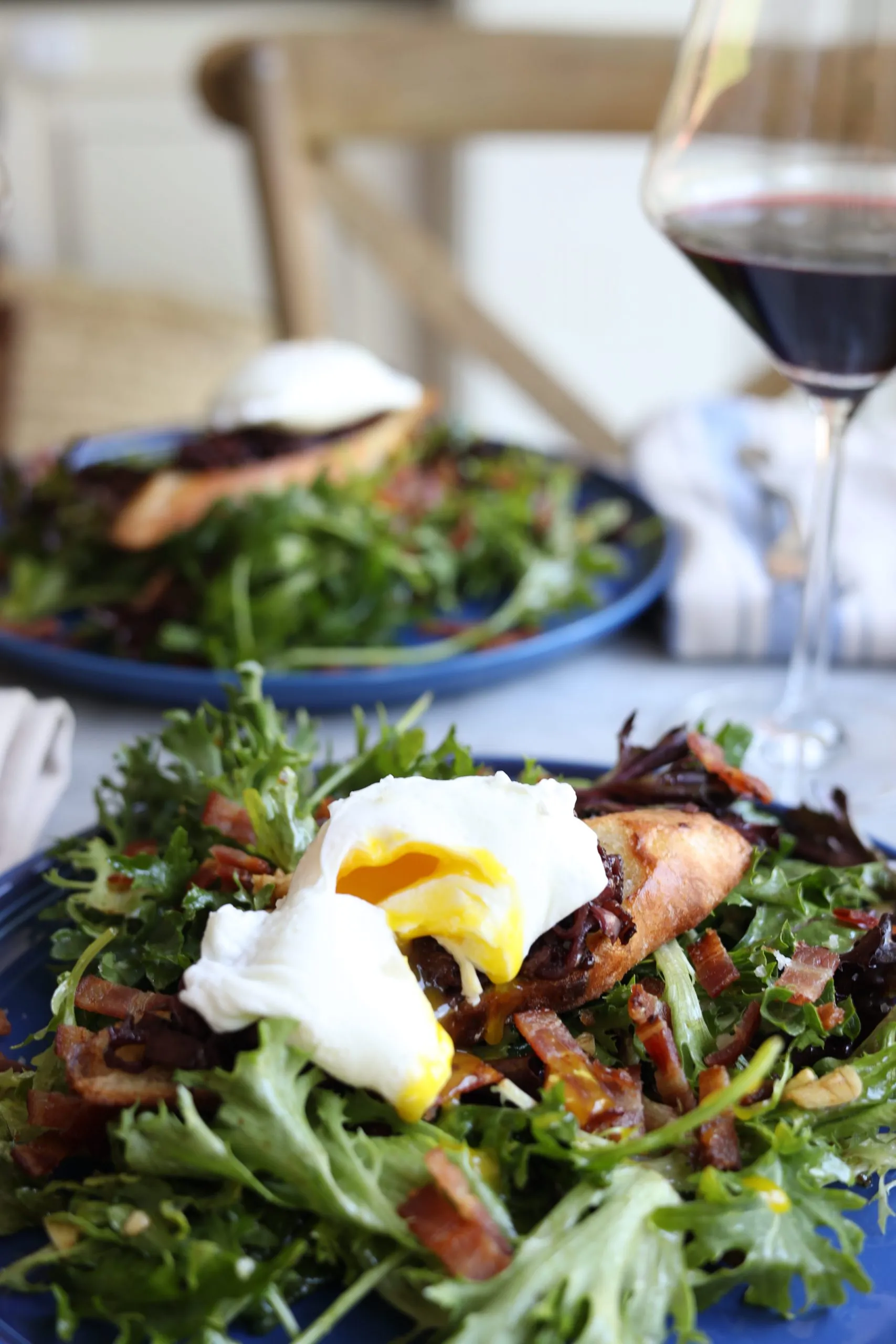 two plates of salade lyonnaise , poached egg, salad and baguette with two glasses of red wine