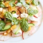 close up of La Salade Tropezienne with shrimp, peaches, cucumbers, goat cheese, basil and cilantro and lemon thyme on a plate with a glass of Rosé wine and peaches