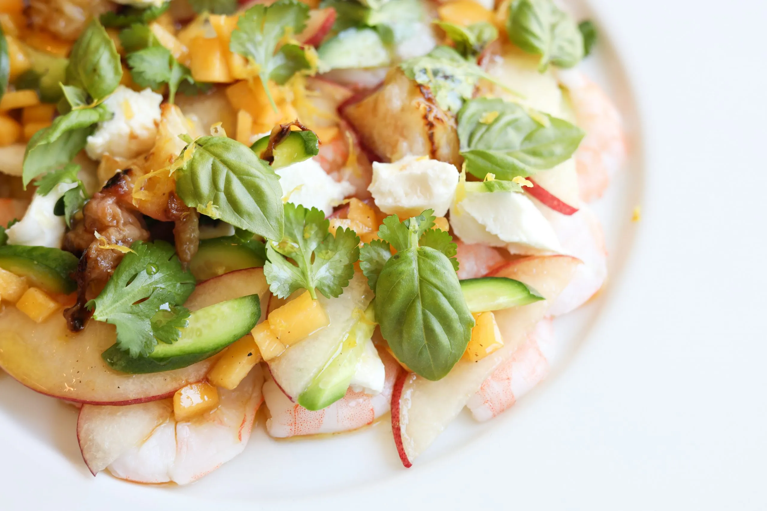 close up of La Salade Tropezienne with shrimp, peaches, cucumbers, goat cheese, basil and cilantro and lemon thyme on a plate with a glass of Rosé wine and peaches