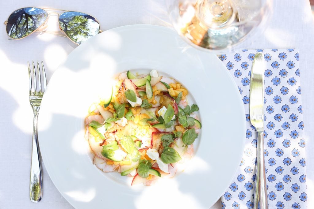 La Salade Tropezienne with shrimp, peaches, cucumbers, goat cheese, basil and cilantro and lemon thyme on a plate with a glass of Rosé wine and peaches
