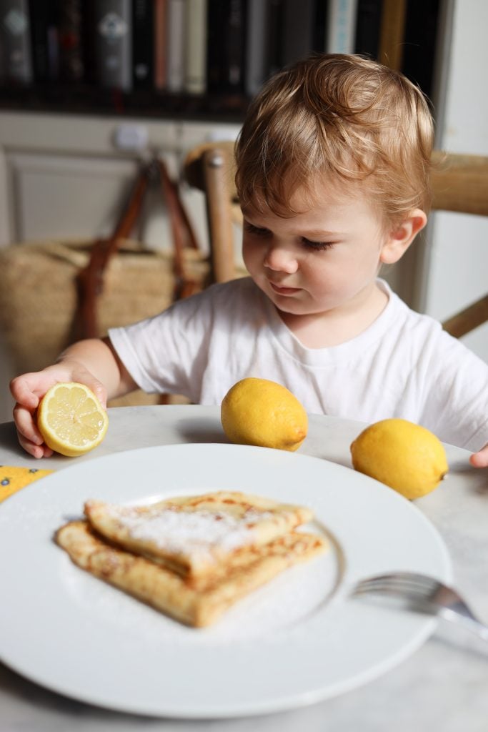 young boy squeezes lemon onto a lemon sugar crepe