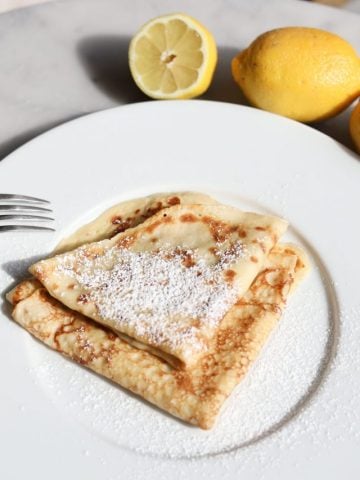 lemons surround a plate of fresh made crรชpes with powdered sugar