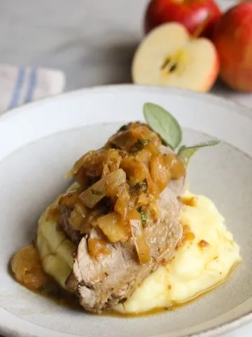 a plate of mashed potatoes topped with sliced roast pork tenderloin with apples and sage