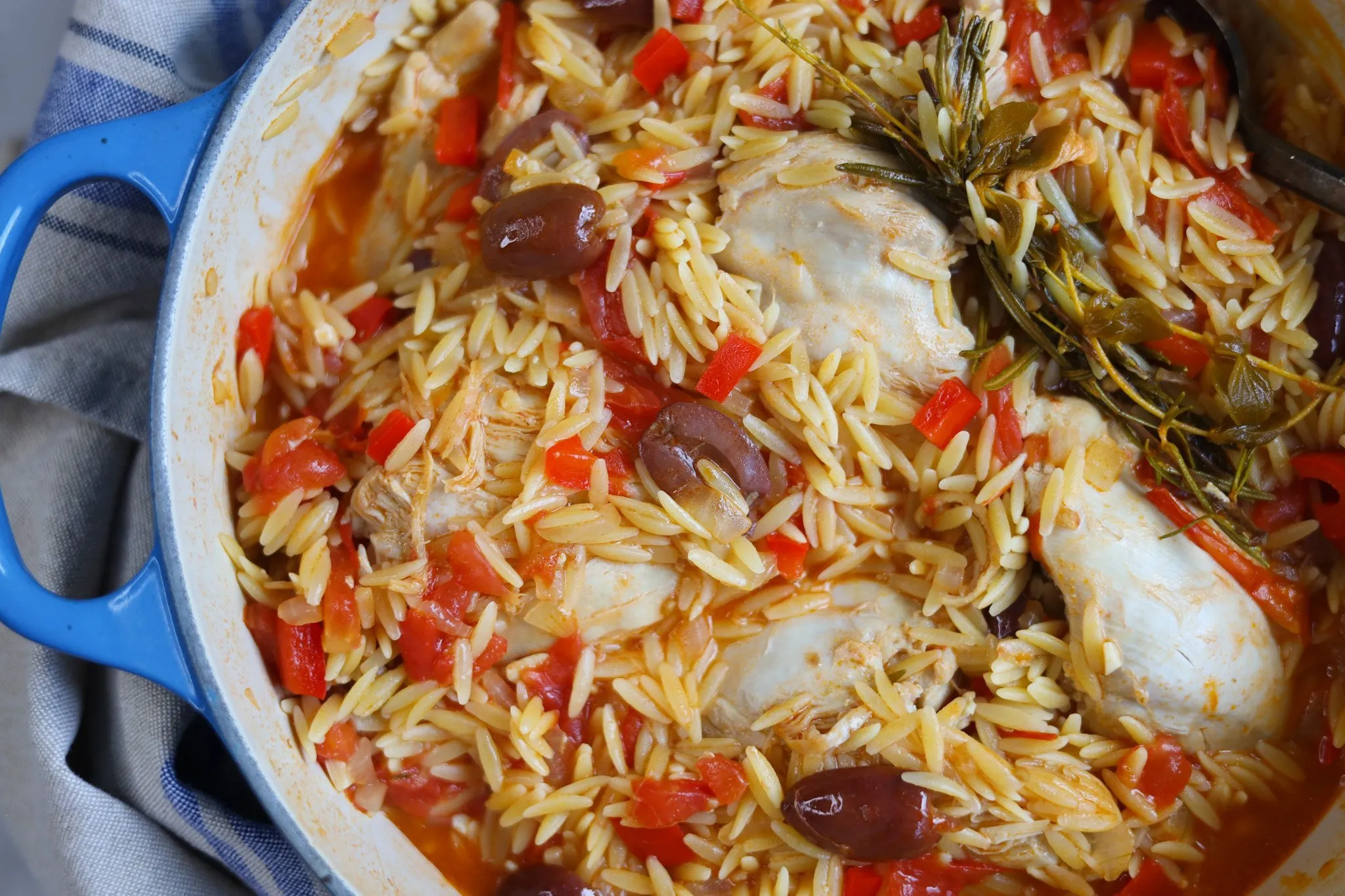 a blue pot with chicken, orzo and olives in a tomato sauce