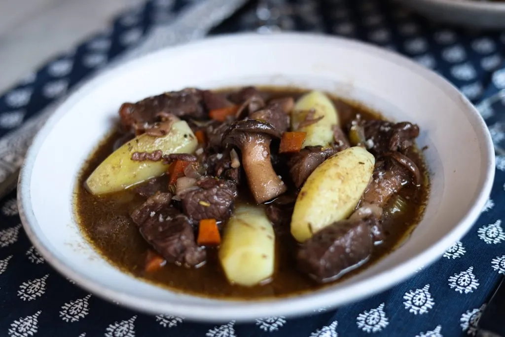 beef bourguignon in a plate with potatoes tournées and a glass of wine