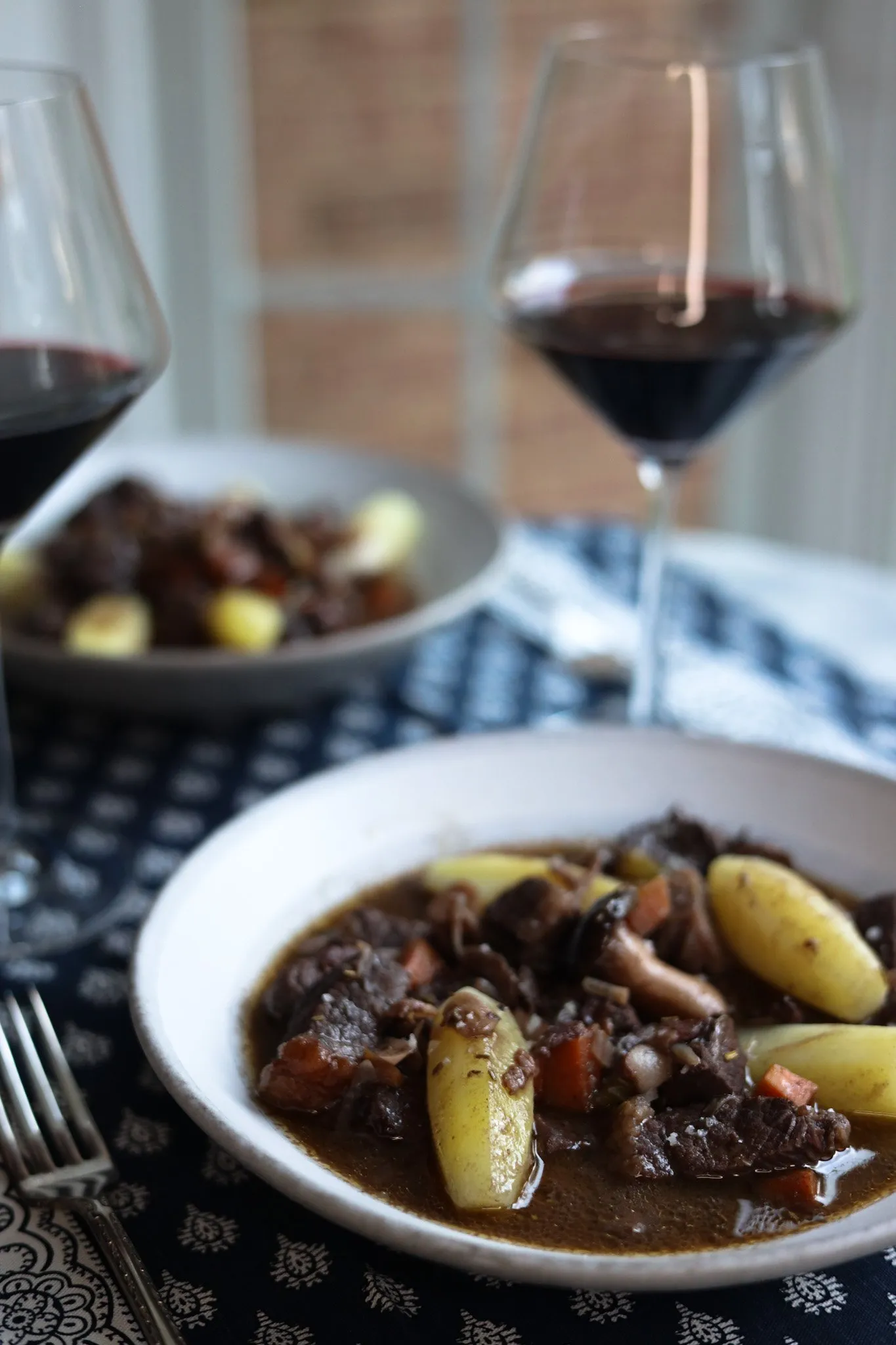 beef bourguignon in a plate with potatoes tournées and a glass of wine