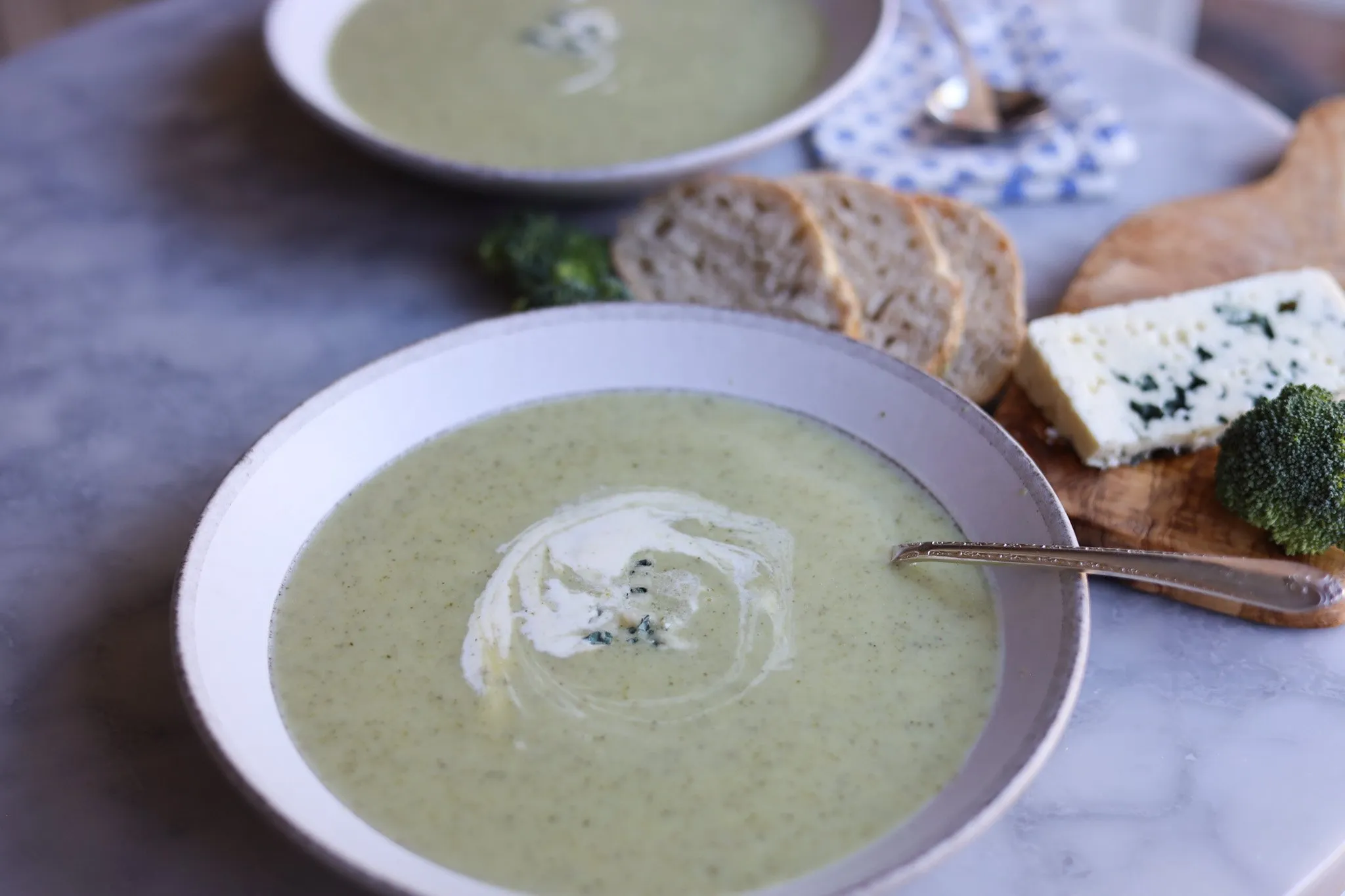 two bowls of broccoli and blue cheese soup on a table with blue cheese and bread