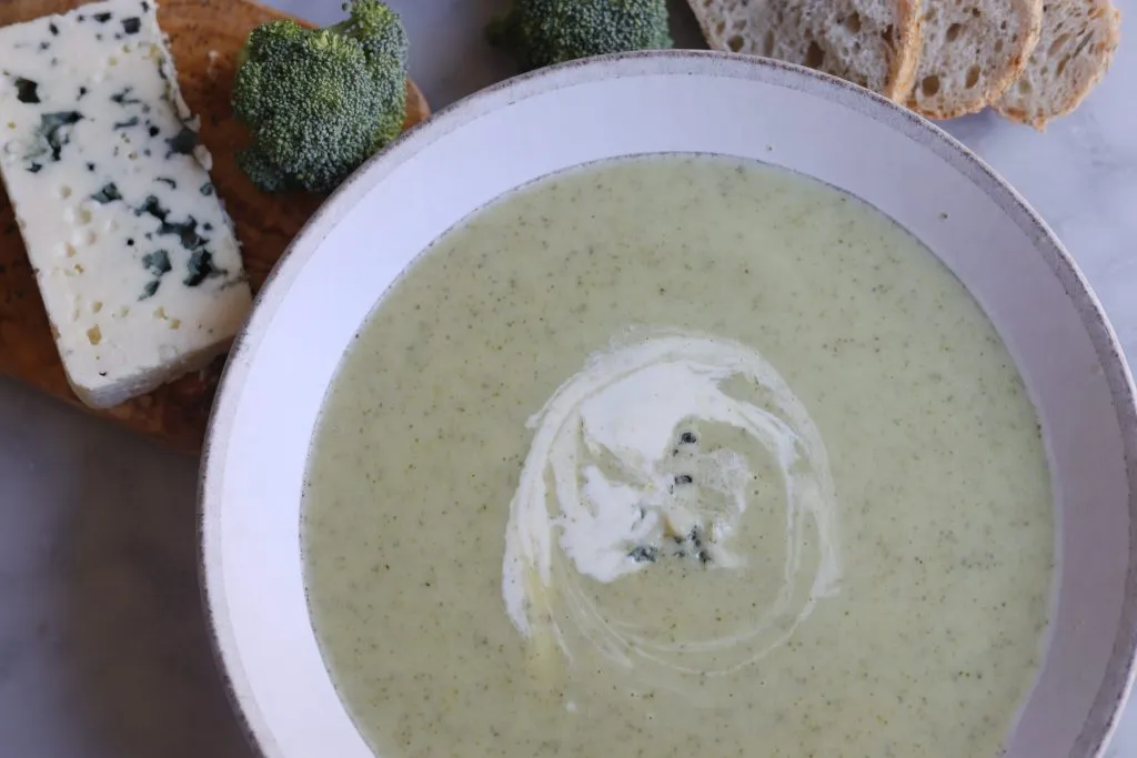 broccoli and blue cheese soup on a table with blue cheese and bread