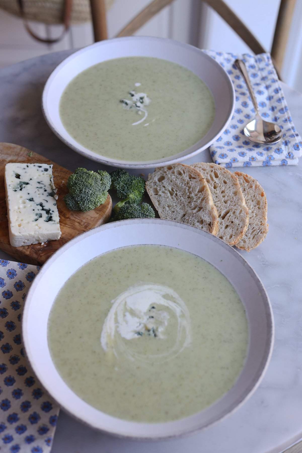 two bowls of broccoli and blue cheese soup on a table with blue cheese and bread