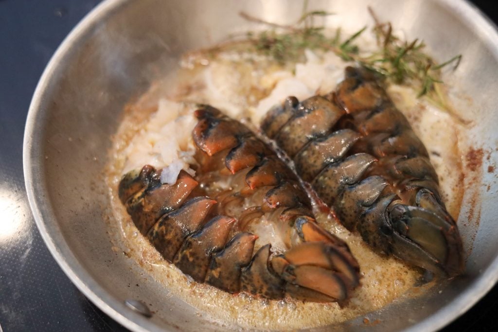 two lobster tails split and poaching in a pan with butter