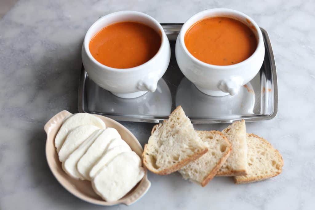 tomato soup gratinee in two bowls with baguette next to it and mozzarella cheese