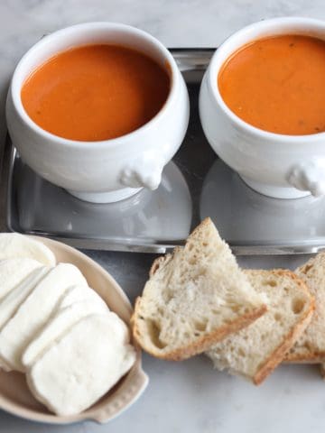tomato soup gratinee in two bowls with baguette next to it and mozzarella cheese