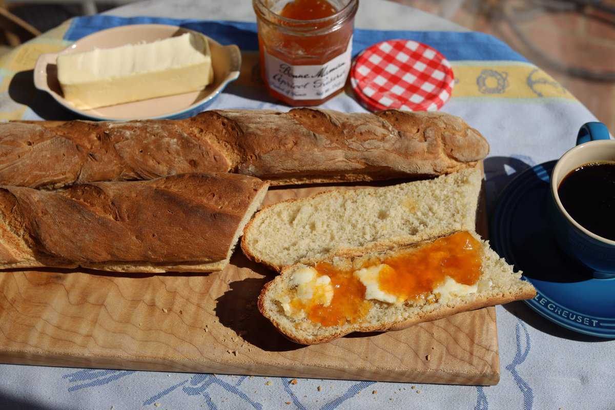 butter and apricot tartine in the sunshine on a table with a fresh baked baguette and a coffee in a blue mug
