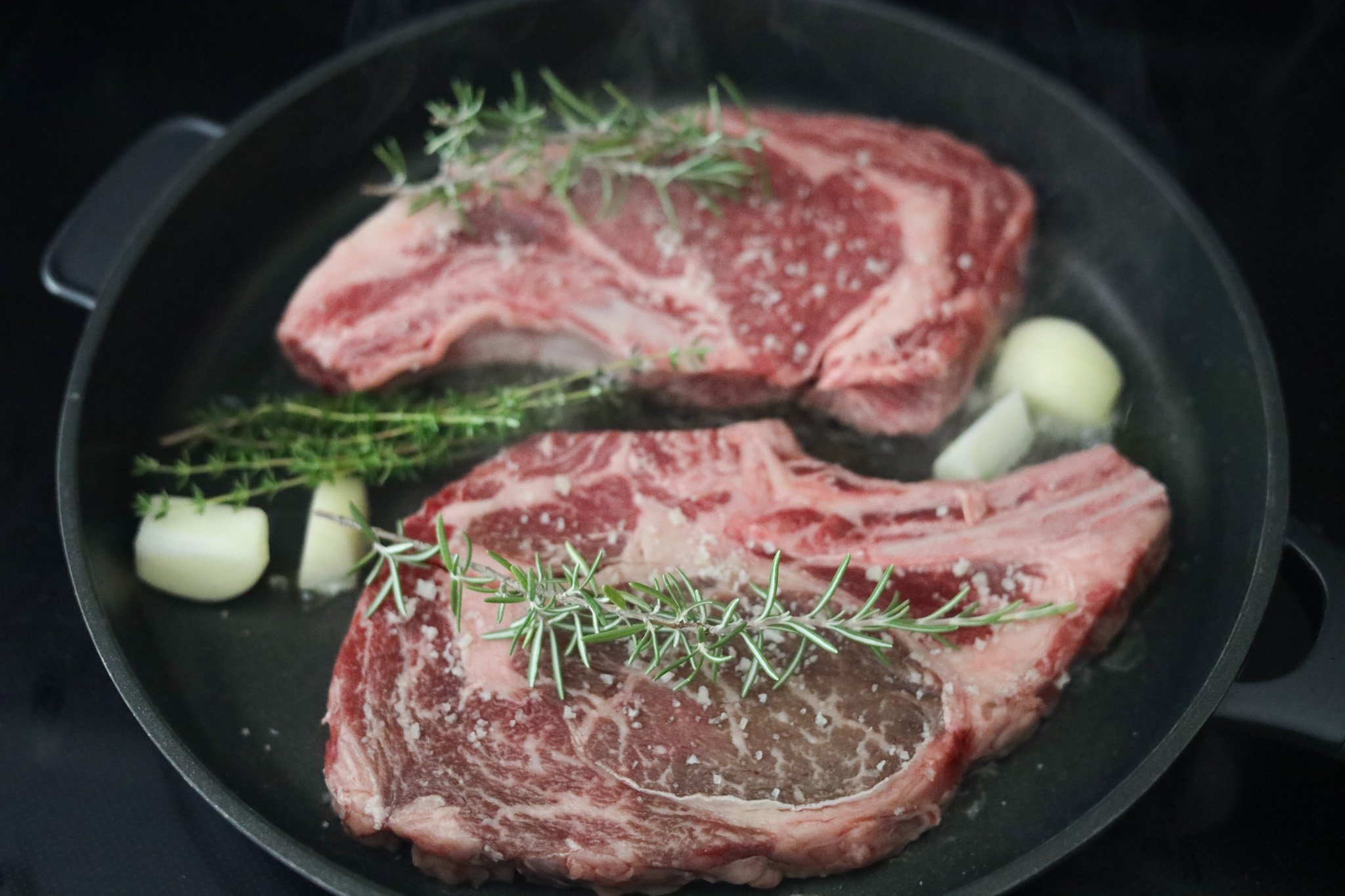 Wagyu rib eye steak cooking in a pan with herbs and garlic