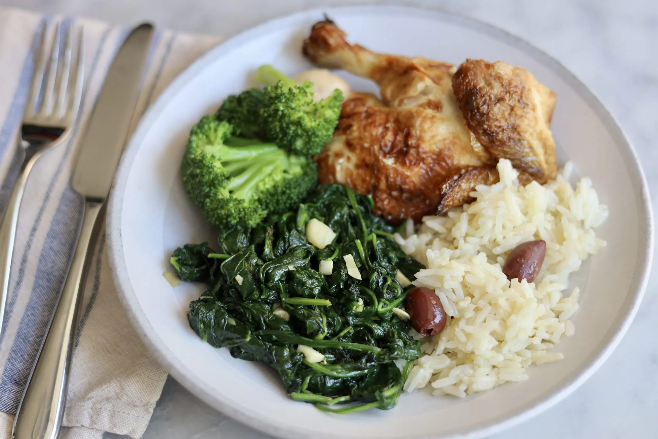 French spinach recipe with garlic and butter on a plate with roast chicken, rice and broccoli
