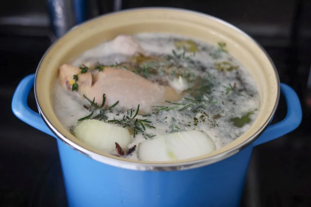chicken poaching in a pot with herbs for chicken stock