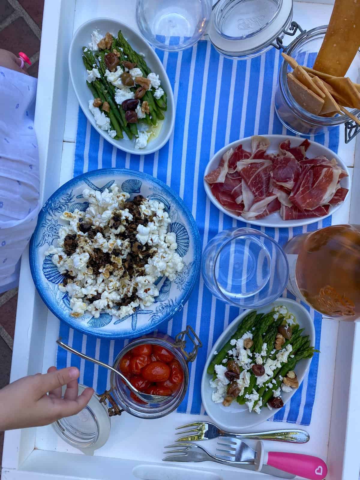 cocktail dinatoire outside. A tray with assortments of bites - truffle popcorn, belotta ham, asparagus, cherry tomatoes and bottle of rose wine.