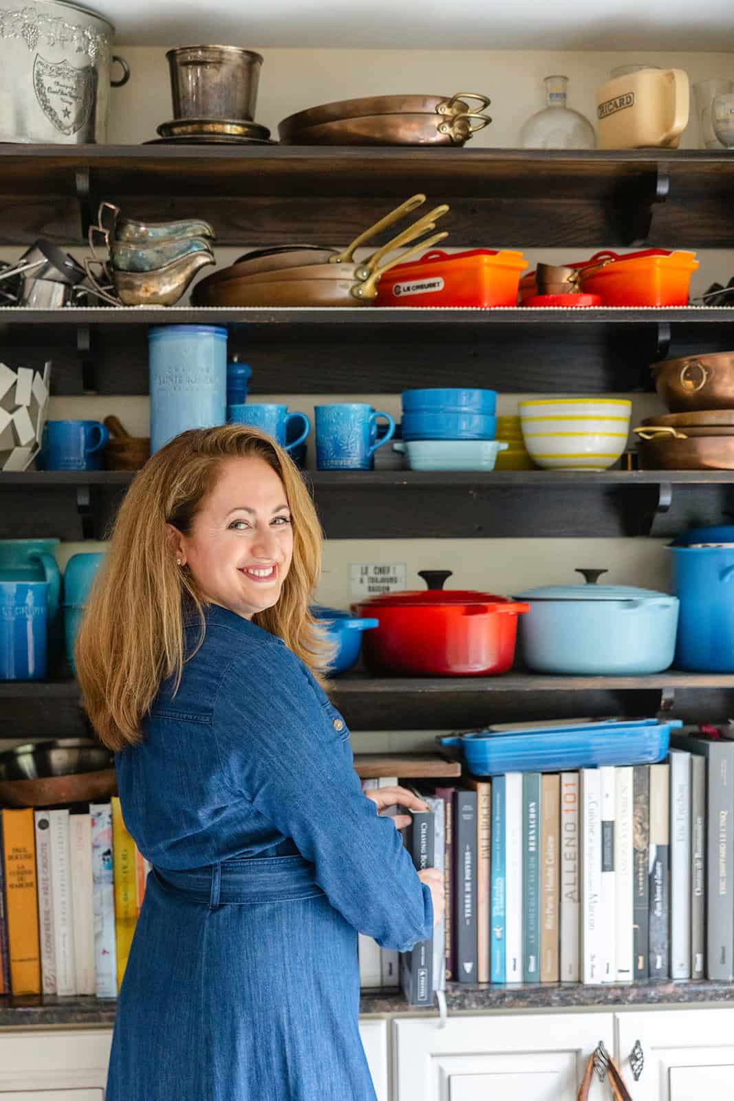 le chefs wife in front of a wall of dutch ovens in her kitchen