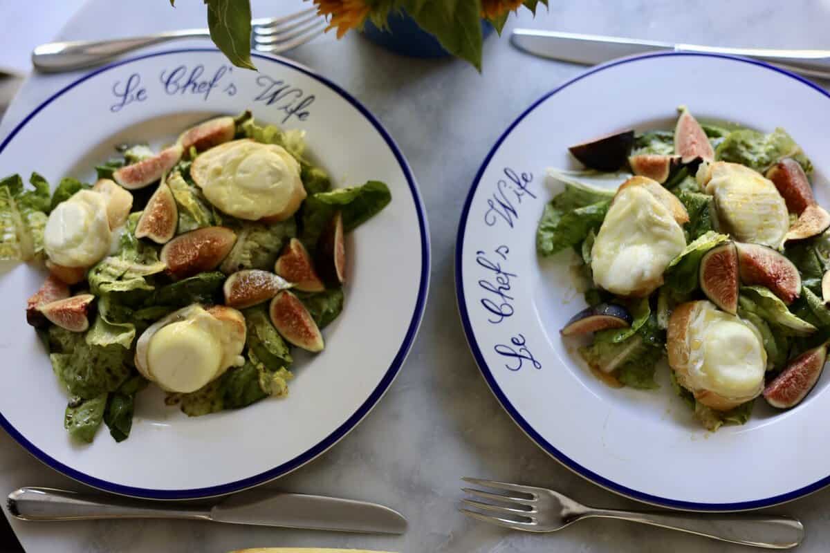 French warm goat cheese salad on two plates with figs and honey over warm goat cheese toasts and salad