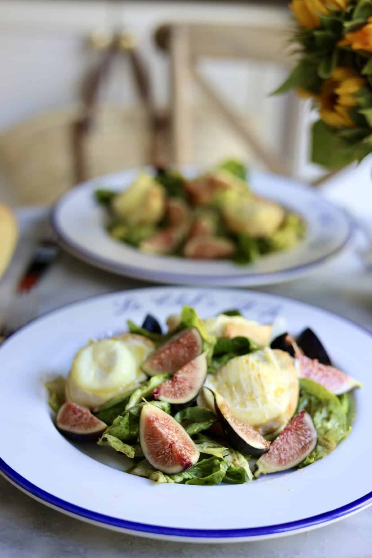 French warm goat cheese salad on a plate with figs and honey over warm goat cheese toasts and salad