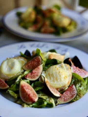 French warm goat cheese salad on a plate with figs and honey over warm goat cheese toasts and salad