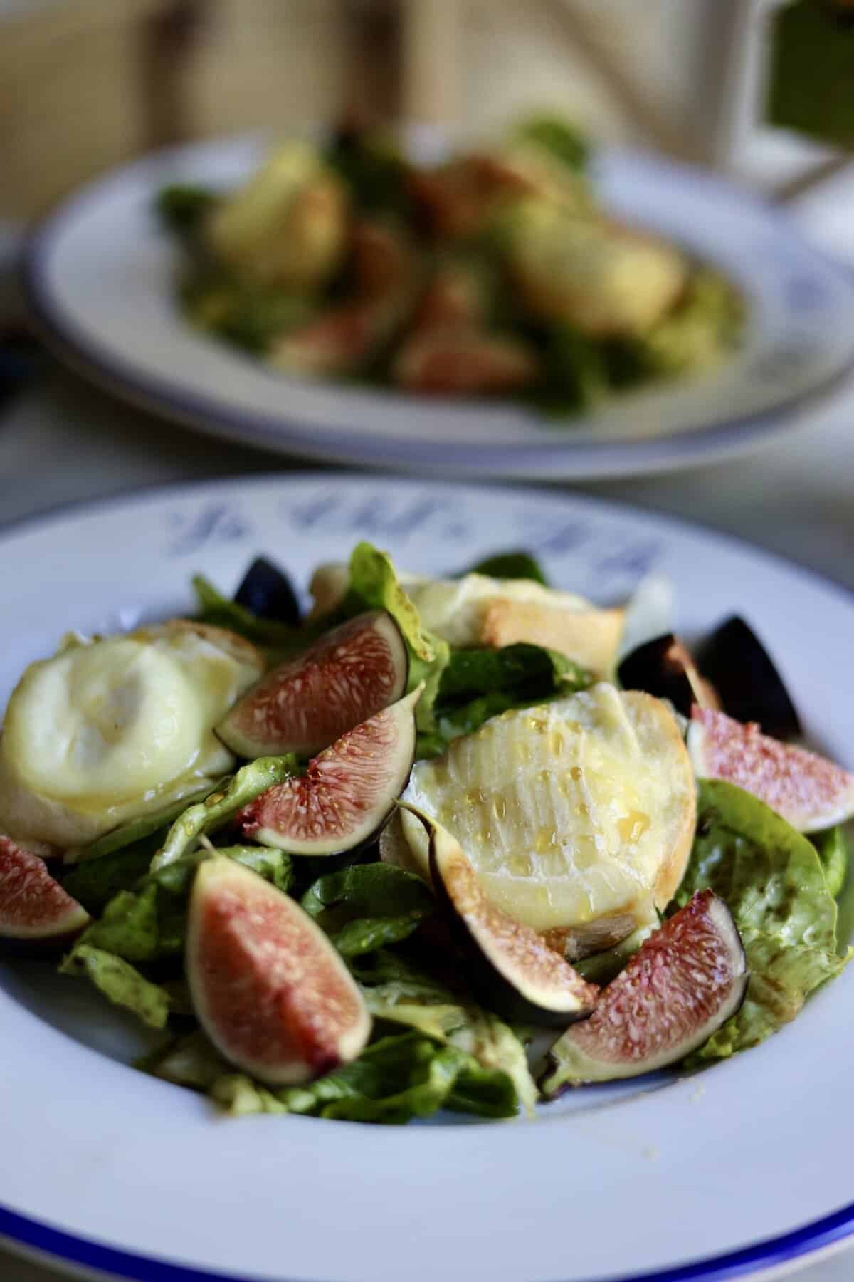 French warm goat cheese salad on a plate with figs and honey over warm goat cheese toasts and salad