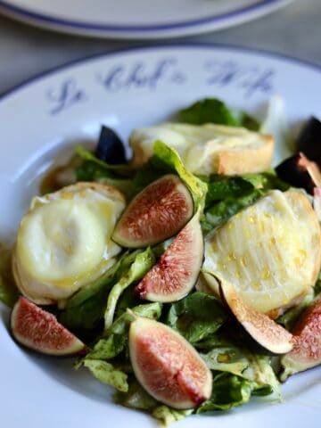 French warm goat cheese salad on a plate with figs and honey over warm goat cheese toasts and salad