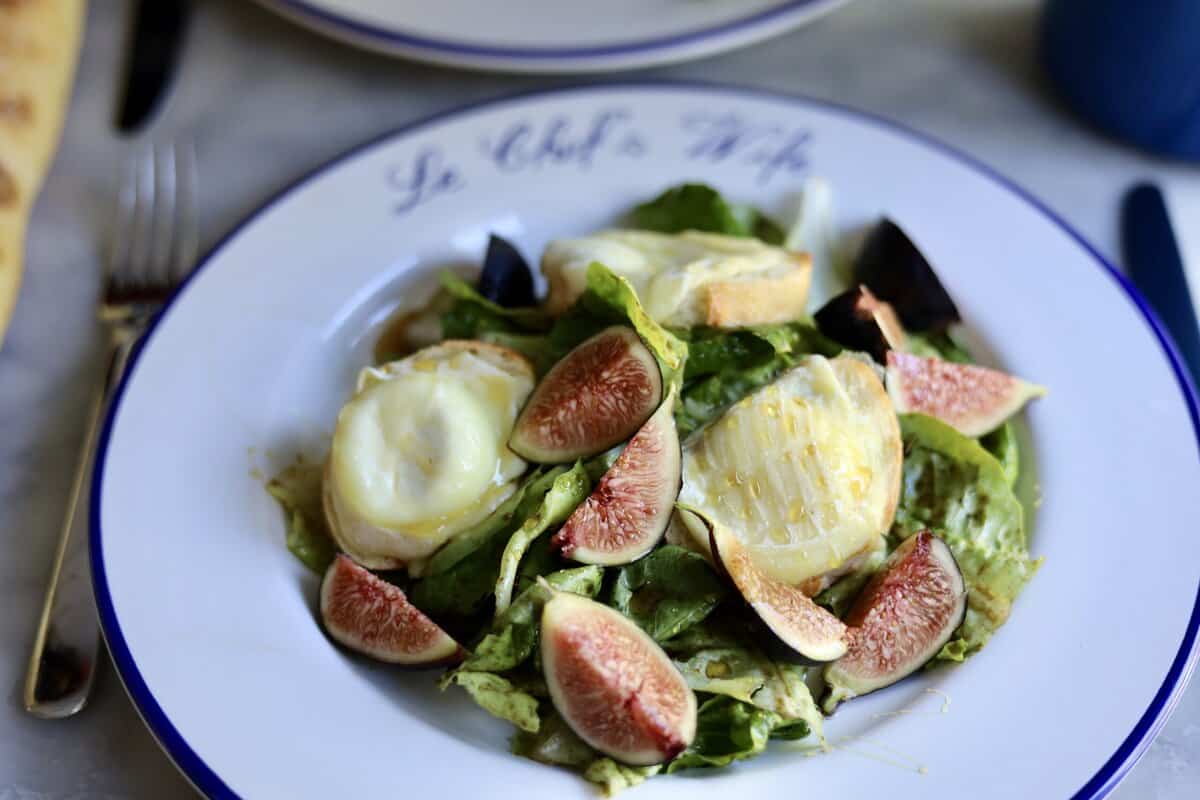 French warm goat cheese salad on a plate with figs and honey over warm goat cheese toasts and salad