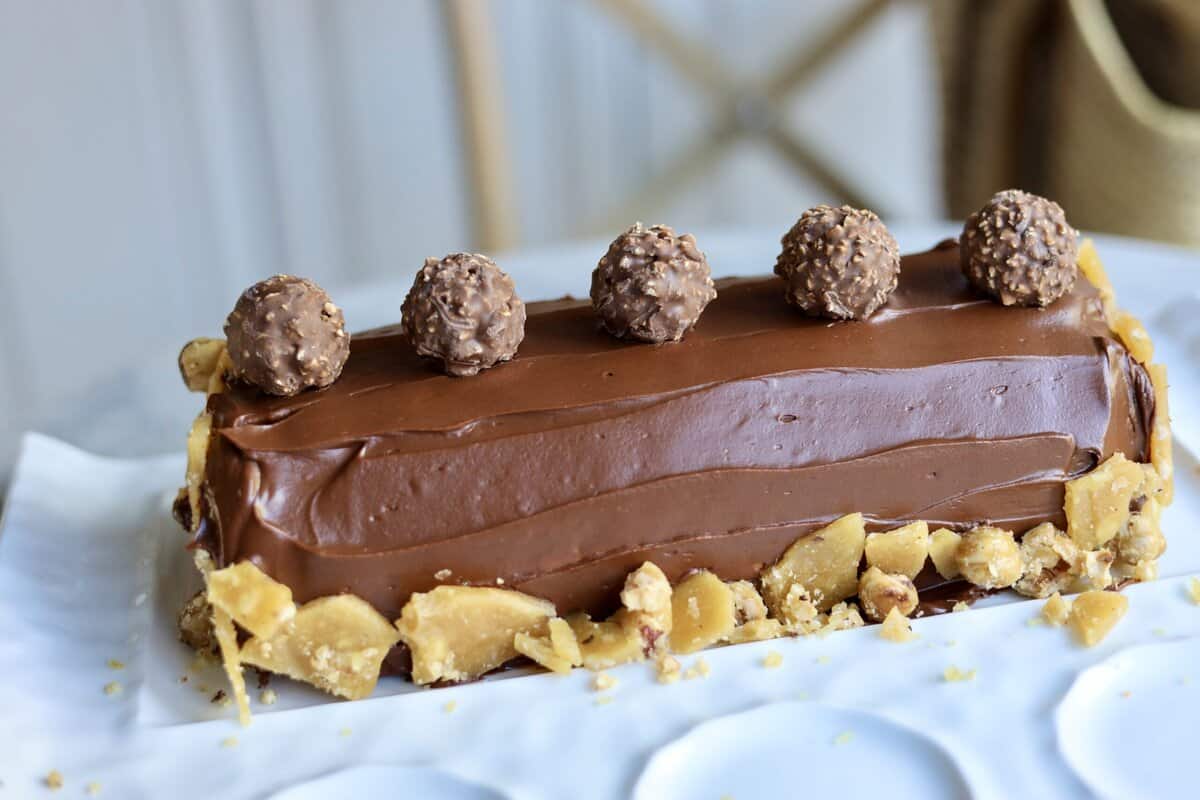 nutella buche de noel topped with ferrero rocher candies and covered in dark chocolate ganache and homemade hazelnut brittle