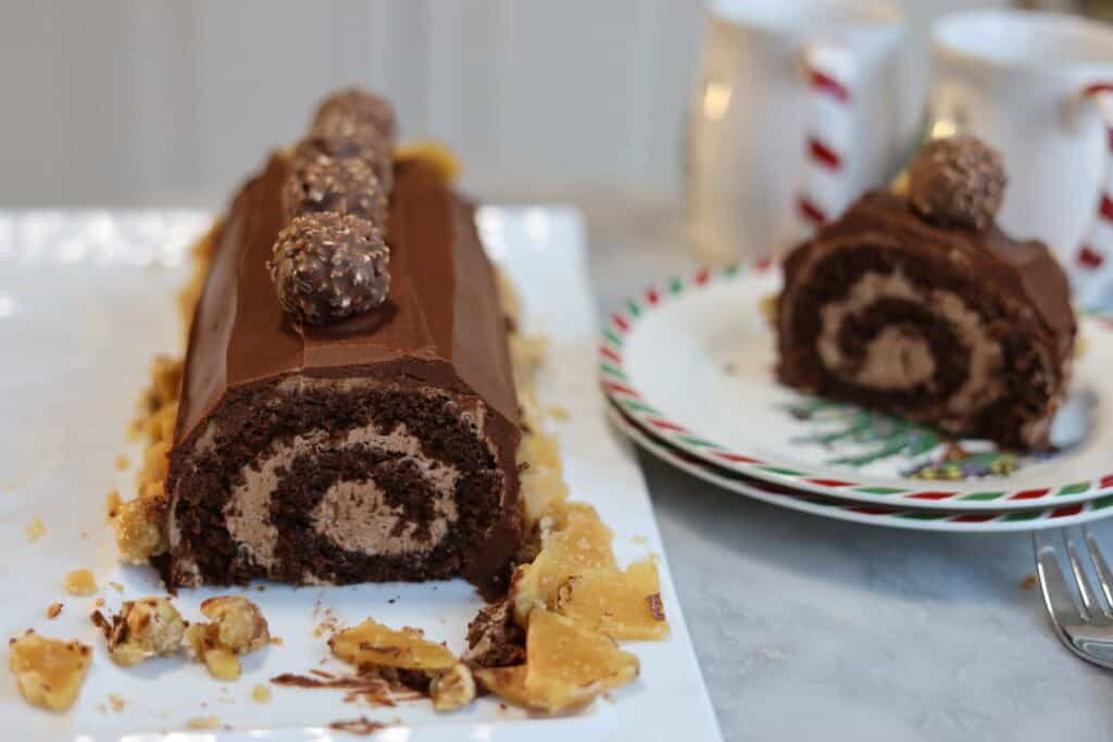 a nutella chocolate buche de noel caked sliced open you can see the perfect swirl of nutella buttercream inside the chocolate cake there is another slice on the plate next to the yule log