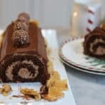 a nutella chocolate buche de noel caked sliced open you can see the perfect swirl of nutella buttercream inside the chocolate cake there is another slice on the plate next to the yule log