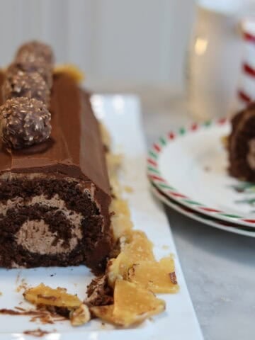 a nutella chocolate buche de noel caked sliced open you can see the perfect swirl of nutella buttercream inside the chocolate cake there is another slice on the plate next to the yule log