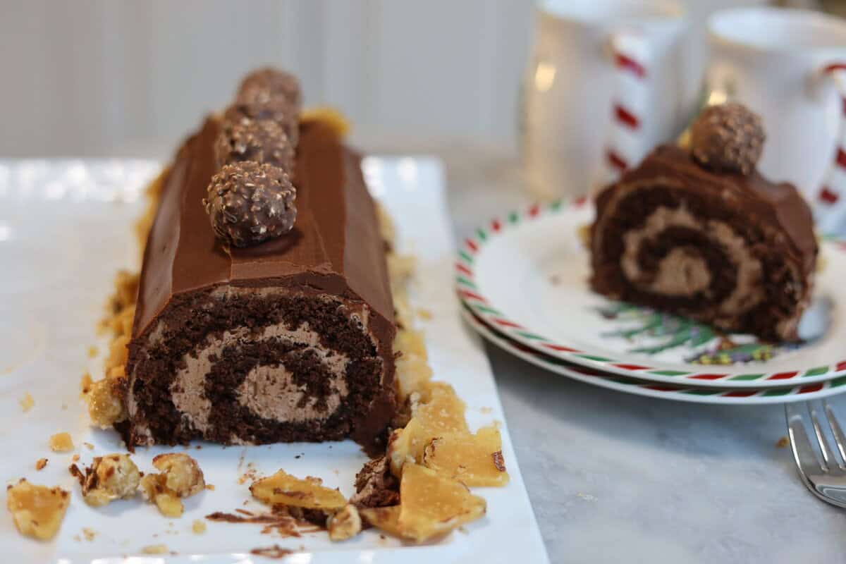 a nutella chocolate buche de noel caked sliced open you can see the perfect swirl of nutella buttercream inside the chocolate cake there is another slice on the plate next to the yule log